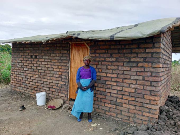   Mpemba stands beside her newly built house, funded by the proceeds from a cash transfer