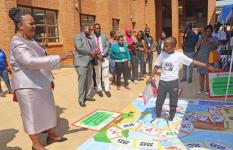 Twelve-Year-Old Arthur demonstrates to the Honourable Minister of Gender, Jean Muonaouza Sendeza, how game boards are used to raise awareness about climate change during her visit to the Save the Children pavilion at the National Children’s Summit on Climate Crisis and Child Rights.